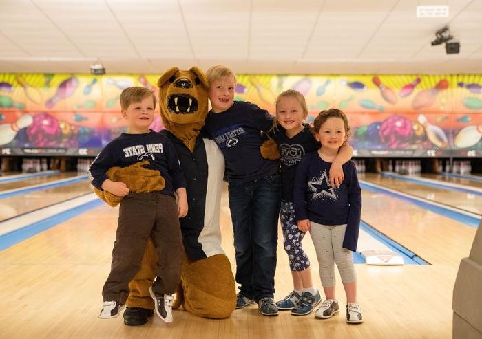 Two young boys and girls stand with Nittany Lion mascot at bowling alley